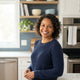 A smiling, diverse woman in a bright, modern kitchen, reflecting a happy and healthy lifestyle.