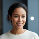 Close-up portrait of a smiling woman in her late 20s, radiating warmth and happiness against a blurred background.